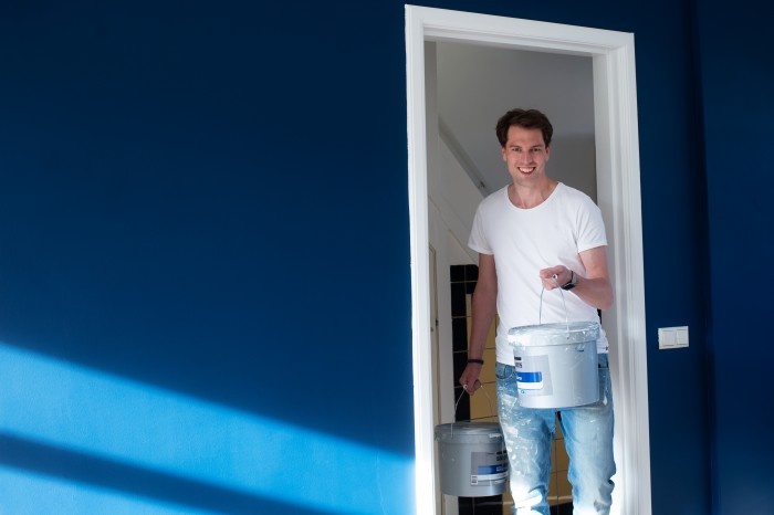 Man in a white shirt holding paint in a blue room