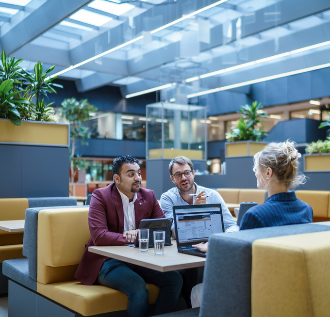 Drie medewerkers zitten aan een tafel met hun laptops