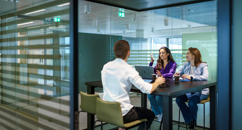 Drie medewerkers zitten aan een hoge tafel met hun laptops