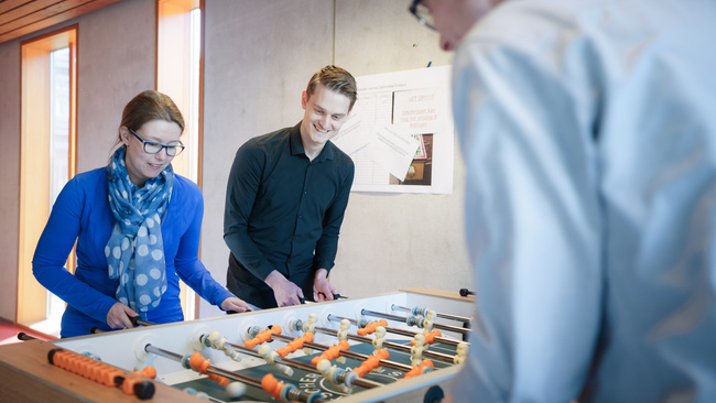 Drie medewerkers aan het spelen achter een voetbaltafel