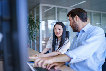 Twee medewerkers zitten aan een bureau en bespreken iets