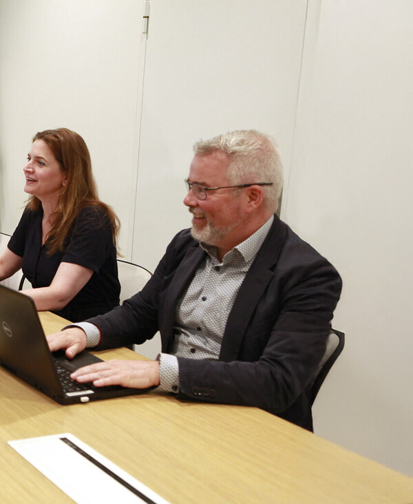 Drie collega's zitten aan vergader bureau in overleg met elkaar.
