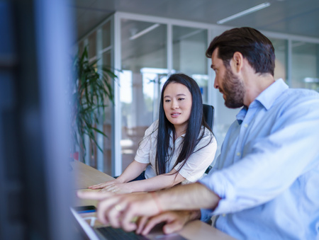 Twee medewerkers zitten aan een bureau en bespreken iets