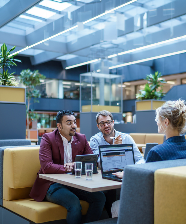 Drie medewerkers zitten aan een tafel met hun laptops