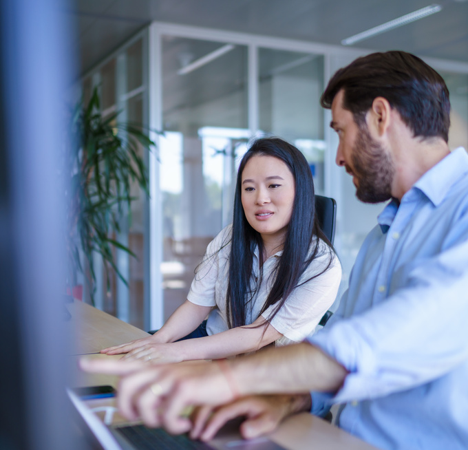 Twee medewerkers zitten aan een bureau en bespreken iets