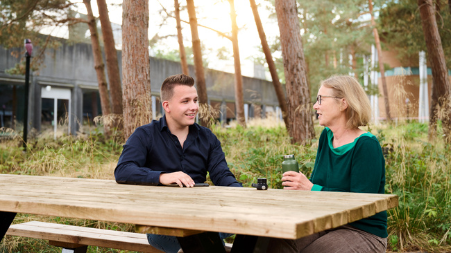 Twee medewerkers zitten buiten aan een tafel