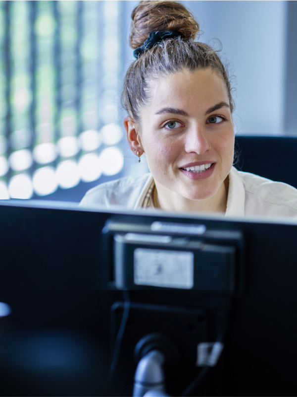 Medewerker zit achter haar laptop en luistert naar een andere medewerker