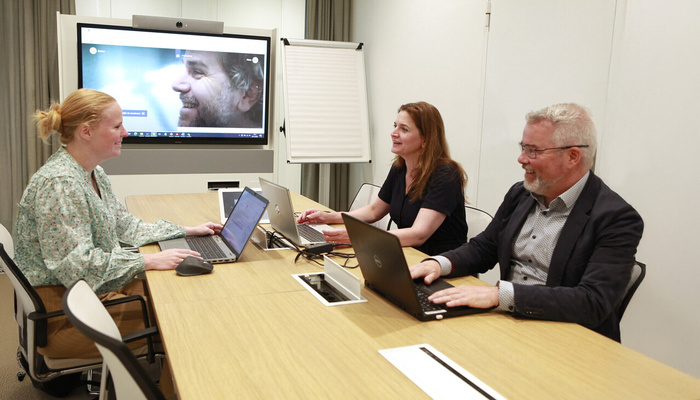 Drie collega's zitten aan vergader bureau in overleg met elkaar.