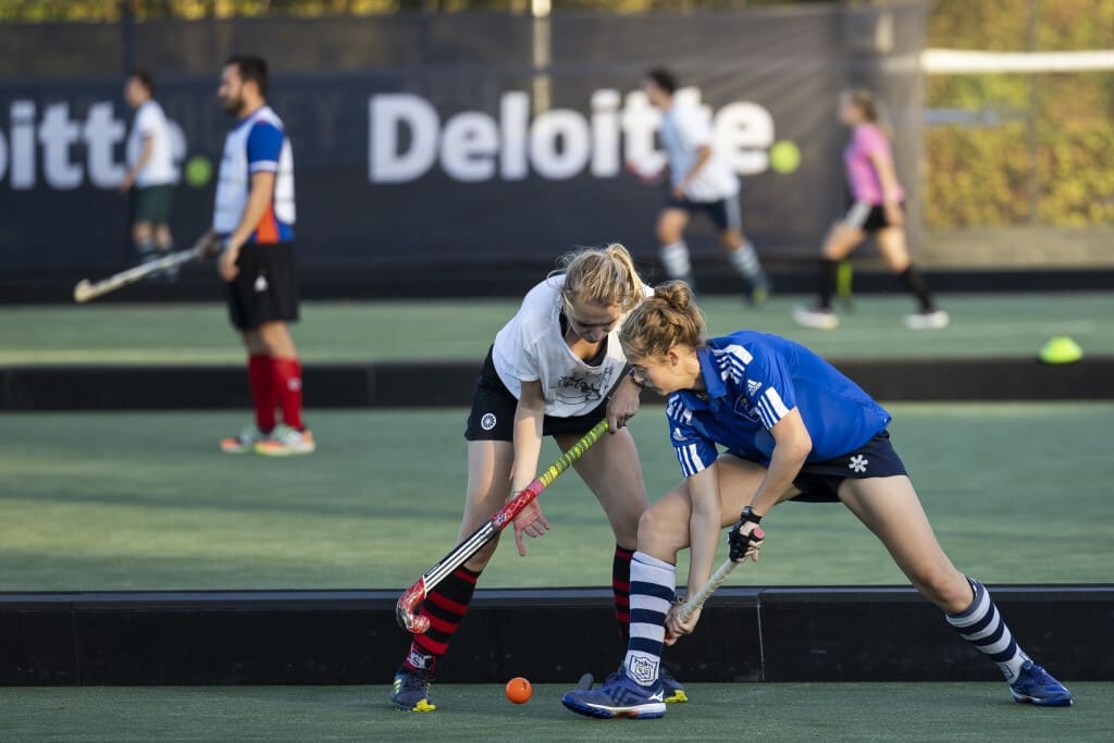Two girls playing hockey in a field.