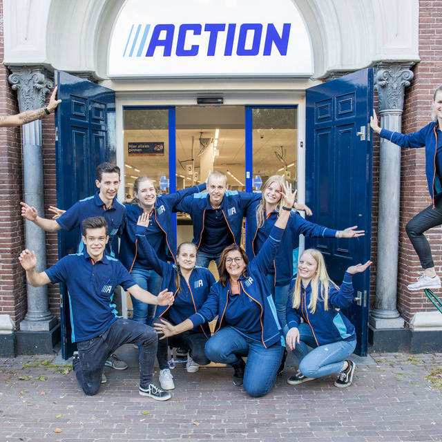 Enthusiastic group of Action employees in front of an Action store
